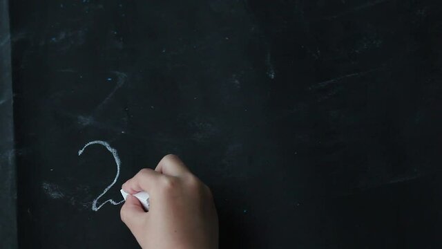 Children is hand writes an example in chalk on a black background. The solution to example two plus two equals four