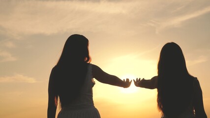 daughter and mother stretch their hands to sun. Happy family mom and daughter in field at sunset. concept of happy family of children . mother and baby are walking in park