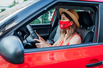 Woman driver sitting in car wearing protective mask during coronavirus pandemic. Stylish young girl driving