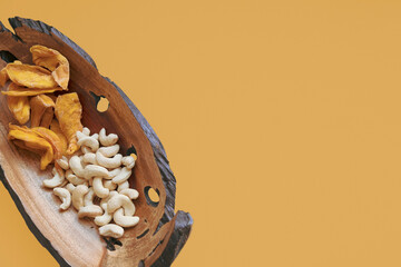 Beautiful wooden plate with natural holes with cashews and dried mango slices on an orange...