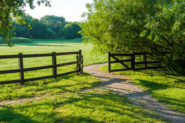 An old wooden cattle gate against the backdrop of a picturesque valley and a meadow with trees in the countryside, on a Sunny summer day.