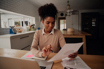 Young female freelancer analysing documents and comparing growth while working on laptop at home during covid-19 lockdown