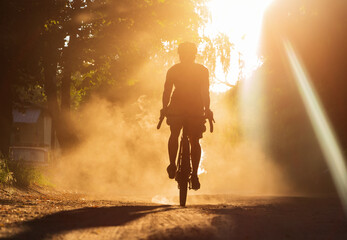 A man riding a bicycle on a gravel road at sunset. A silhouette of a cyclist on a gravel bike in a...