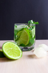 Refreshing mint cocktail mojito with rum and lime, cold drink or beverage with ice on black background