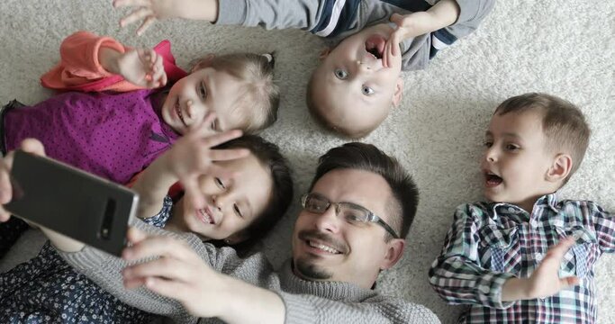 A happy family are talking on a video call on a mobile phone. Father and children lies on the carpet and takes a selfie.