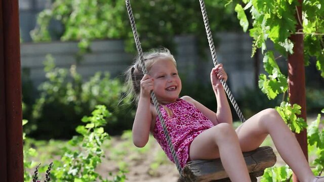 Cheerful girl riding in the courtyard of the house on a makeshift swing