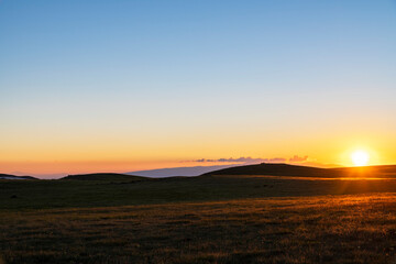 Fototapeta na wymiar Beautiful sunset landscape. The green field and mountains illuminates the sun rays.