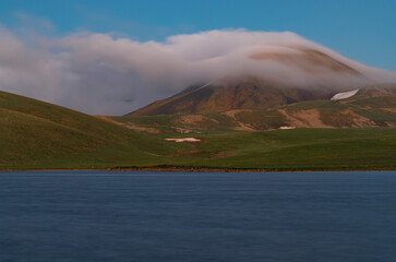 Beautiful long exposhure landscape with alpine lake mountains and green hills.