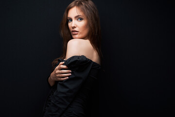 portrait of a beautiful woman in a dark dress posing on a dark background, beautiful brown hair looking from shoulder