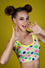 Young happy fitness girl with sporty body posing at studio on a yellow background.