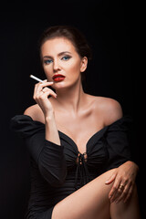 Fototapeta premium beautiful girl on a dark background in a dark dress looks into the frame with a cigarette in her hands and a hairdresser male hands