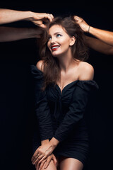 beautiful woman smiles with beautiful brown hair in a dark dress on a dark background and with men's hands makes a hairstyle