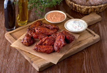 Roasted chicken wings in barbecue sauce and parsley on a wooden board on a table. With copy space. Tasty snack for beer on a dark background
