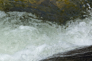closeup of river water splashing over rock forming white water and lots of bubbles