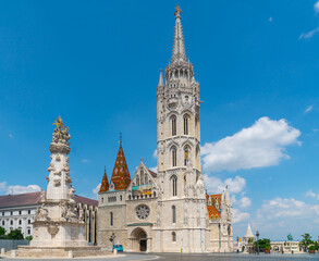 Fototapeta na wymiar Budapest, Hungary - june 27th 2020 - Exterior of the Matthias Church, with the Holy Trinity Statue in front during Corona time on a sunny day with some tourists visiting the church