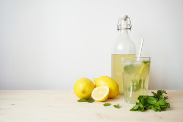 Lemonade in glass and bottle on wooden table. Lemonade or mojito cocktail with lemon and mint, cold refreshing drink or beverage with ice. Copy space for your text