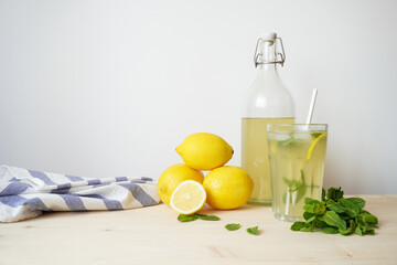 Lemonade in glass and bottle on wooden table. Lemonade or mojito cocktail with lemon and mint, cold refreshing drink or beverage with ice. Copy space for your text