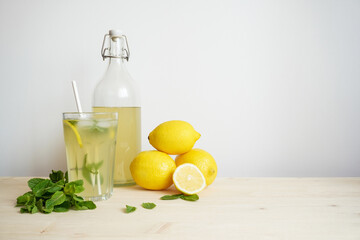 Lemonade in glass and bottle on wooden table. Lemonade or mojito cocktail with lemon and mint, cold refreshing drink or beverage with ice. Copy space for your text