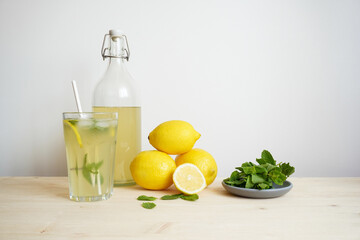 Lemonade in glass and bottle on wooden table. Lemonade or mojito cocktail with lemon and mint, cold refreshing drink or beverage with ice. Copy space for your text