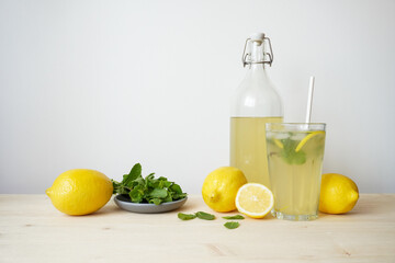 Lemonade in glass and bottle on wooden table. Lemonade or mojito cocktail with lemon and mint, cold refreshing drink or beverage with ice. Copy space for your text