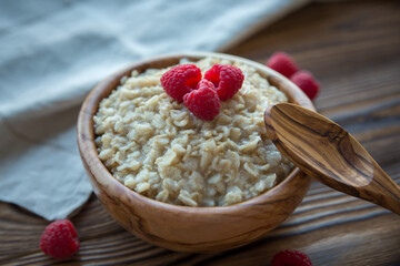 Oatmeal porridge with raspberry berries in a wooden bowl on a wooden background. Useful breakfast, diet.