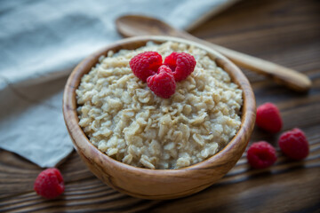 Oatmeal porridge with raspberry berries in a wooden bowl on a wooden background. Useful breakfast, diet.
