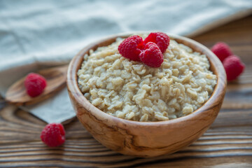 Oatmeal porridge with raspberry berries in a wooden bowl on a wooden background. Useful breakfast, diet.