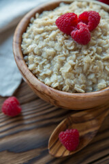 Oatmeal porridge with raspberry berries in a wooden bowl on a wooden background. Useful breakfast, diet.