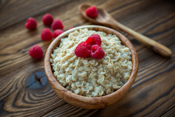 Oatmeal porridge with raspberry berries in a wooden bowl on a wooden background. Useful breakfast, diet.