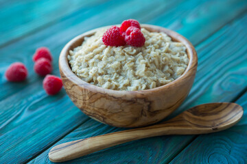 Oatmeal with raspberry berries in a wooden bowl on a blue background