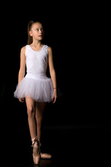 Cute little girl in a tutu and pointe shoes is dancing in the studio on a black background.