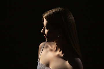 Portrait of a young mysterious girl 25 years old on a dark background in contour lighting.Modesty...