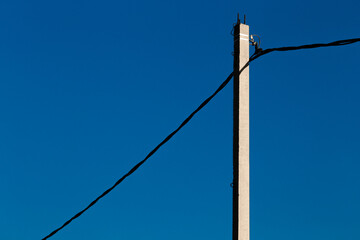 Concrete pole with electric wire against a blue sky