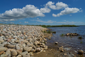 gravel stones at the dam in the lake Filsø (Denmark) on a sunny summer day with vivid blue sky an scenic clouds