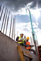 Men in hardhat and yellow and orange jacket posing on building site