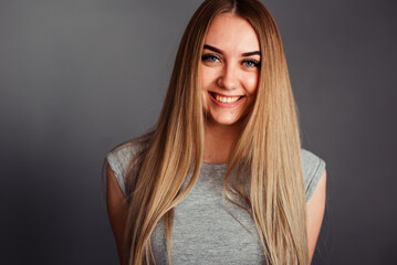 A girl with blue eyes smiles into the frame, hands behind her back on a gray background