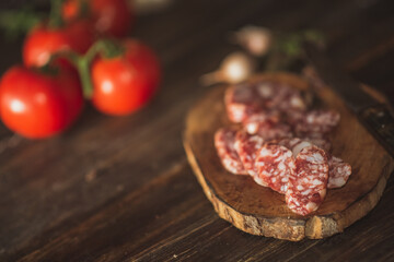 Slices of salami with tomatoes on a cutting board on a wooden table. Selective focus..