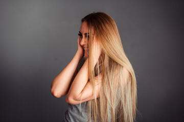 A long-haired girl stands sideways and emotionally laughs at a plain gray background in a T-shirt...
