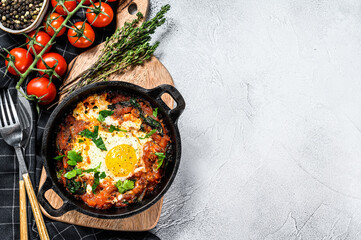 Homemade shakshuka, fried eggs, onion, bell pepper, tomatoes and parsley in a pan.  Gray background. Top view. Copy space