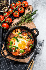 Homemade shakshuka, fried eggs, onion, bell pepper, tomatoes and parsley in a pan.  Gray background. Top view