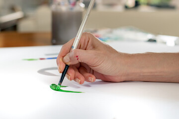 Close-up of an artist hand painting on paper with acrylic holding a painbrush.