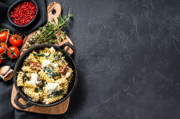 Fusilli pasta with spinach, dried tomatoes and ricotta cheese ia a pan. Black background. Top view. Copy space