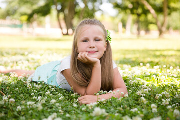 Naklejka na ściany i meble smiling child girl lies on grass in the park on a hot summer day