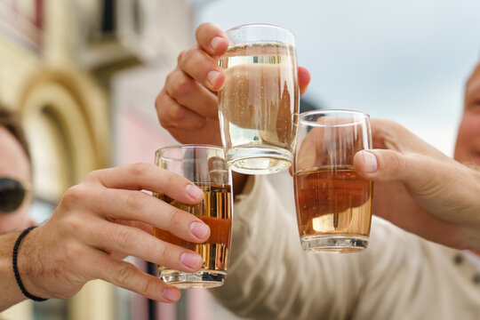 Close up on hands of unknown people holding glasses toasting - Caucasian men celebrating with wine and soda alcohol drink spricer popular in balkan countries - close up front view in day outdoor