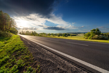 Empty asphalt road in rural landscape at dramatic sunset - obrazy, fototapety, plakaty