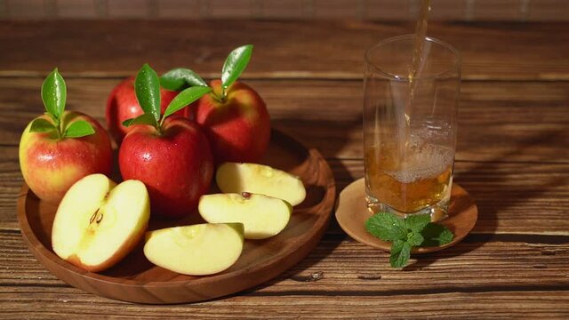 Apple juice. Slow motion shot of pouring apple juice in glass and a red apple on a wooden tray.