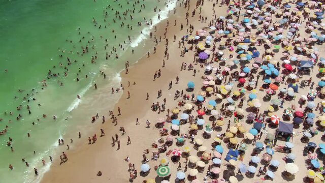 Rio de Janeiro, Brazil, aerial static shot showing Copacabana Beach with colourful sun umbrellas and people bathing in the ocean during summer.
