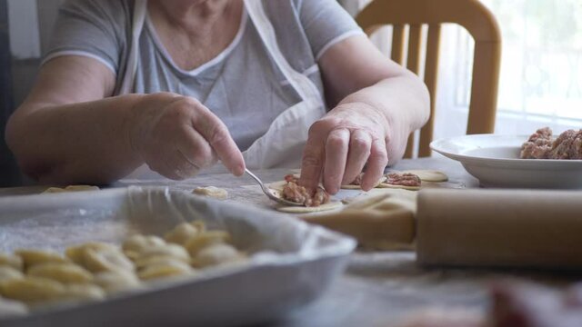 Beautiful elderly woman with wrinkled hands prepares dough on kitchen table. Knife, minced meat and condiments for pies. shallow depth of field