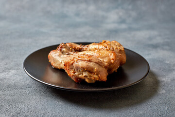 Three baked chicken drumsticks on a black plate