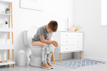 Little boy sitting on toilet bowl in restroom